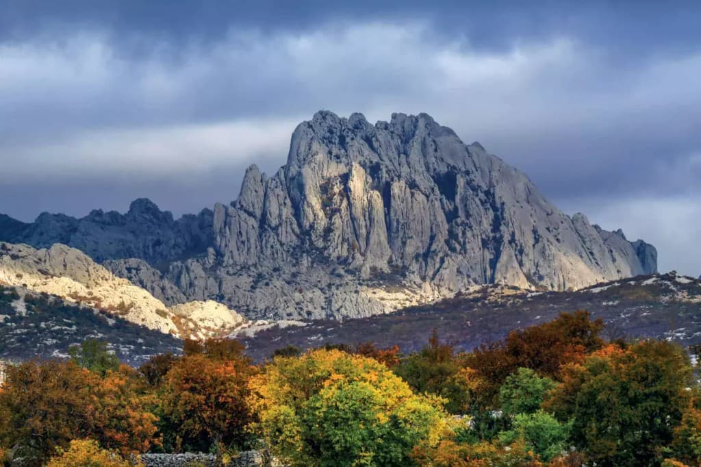 Autumn view of the Velebit massif above coloured forest under dramatic clouds